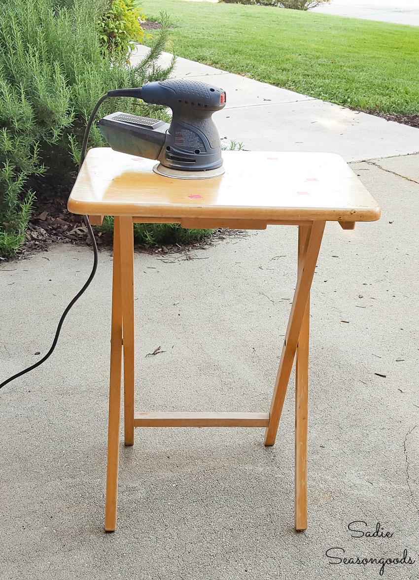 Using an orbital sander to remove the lacquer from a wooden tray table