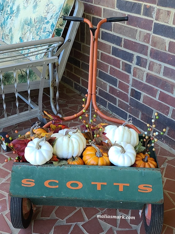filling a fertilizer spreader with pumpkins and leaves for fall porch decor
