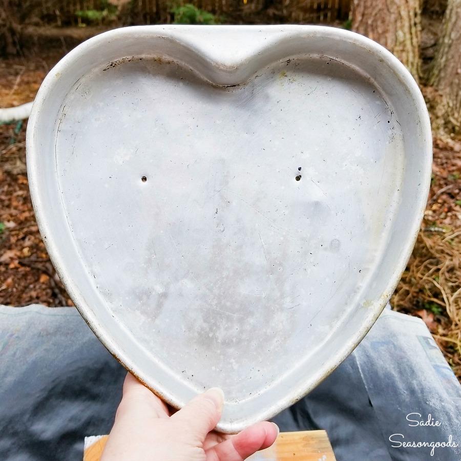 Drilling holes through the heart shape cake pans before upcycling into heart decorations