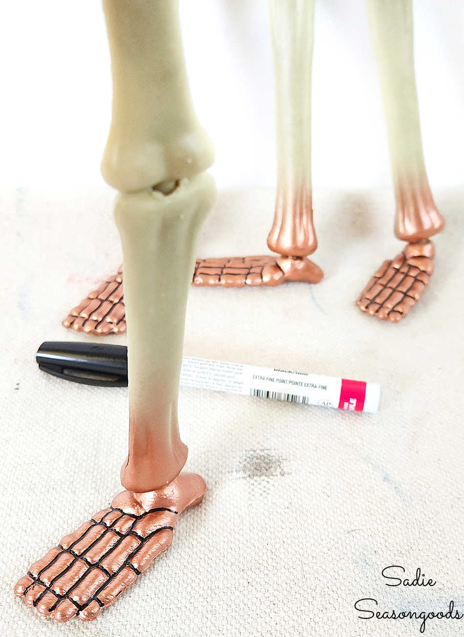 using a black paint pen to color in between the bones on plastic skeleton feet